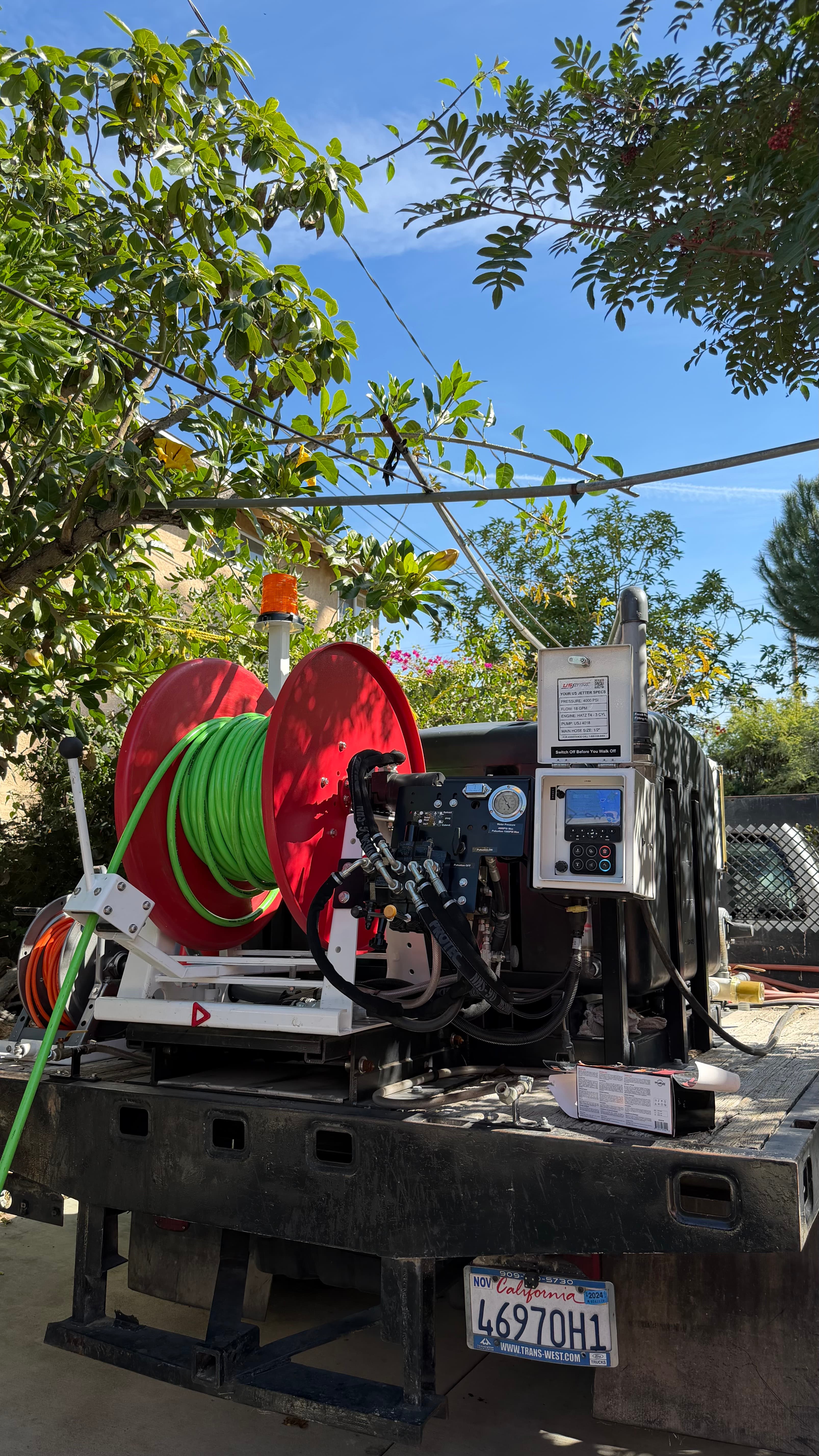 Sewer jetting equipment with a red reel and green hose on a flatbed truck.